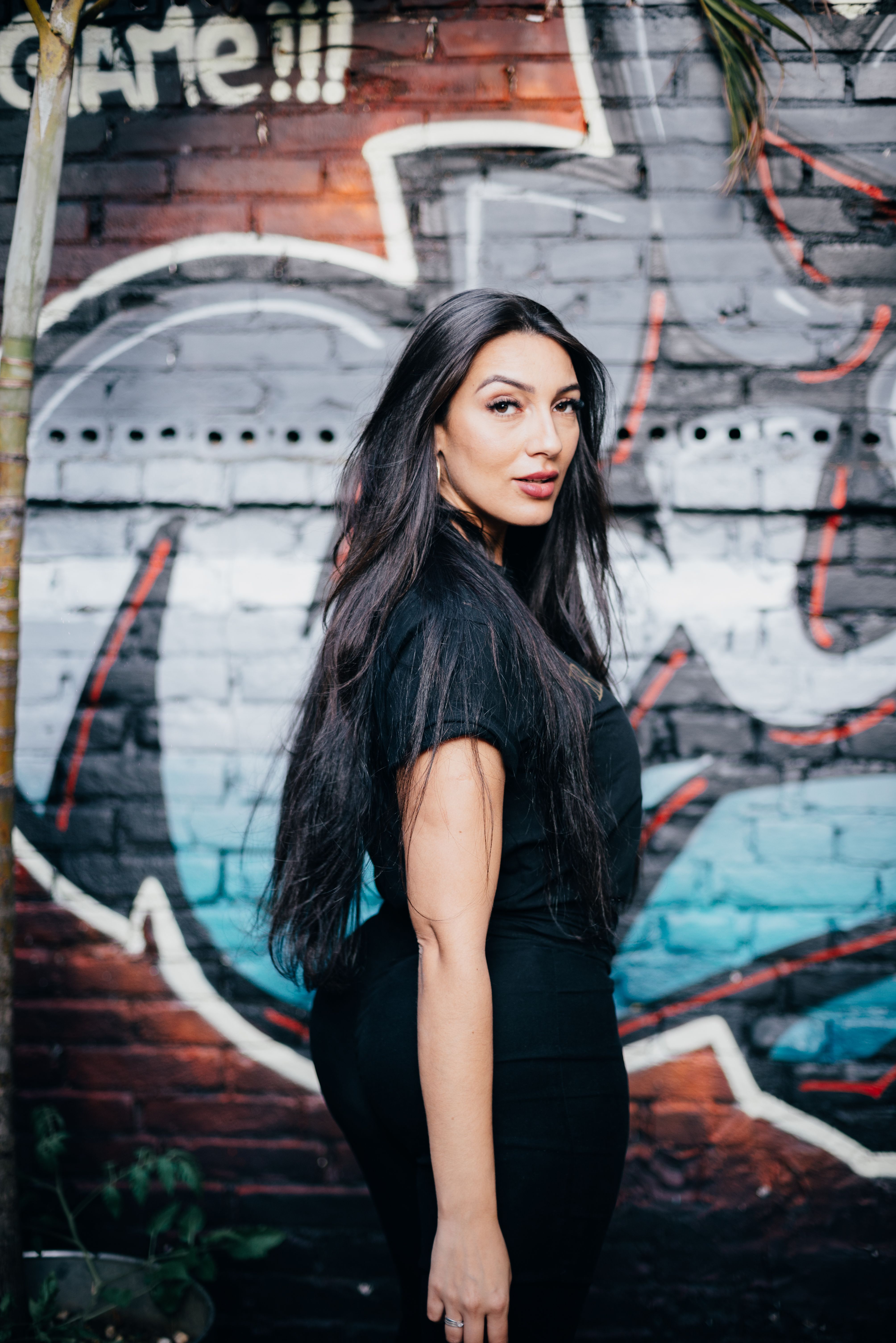 Elegant woman with long black hair posing against vibrant graffiti mural outdoors.