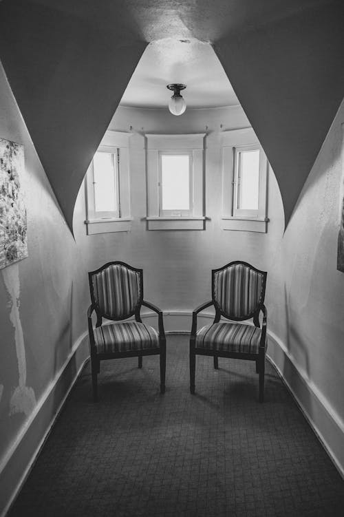 Grayscale Photo of Wooden Armchairs inside a Narrow Room