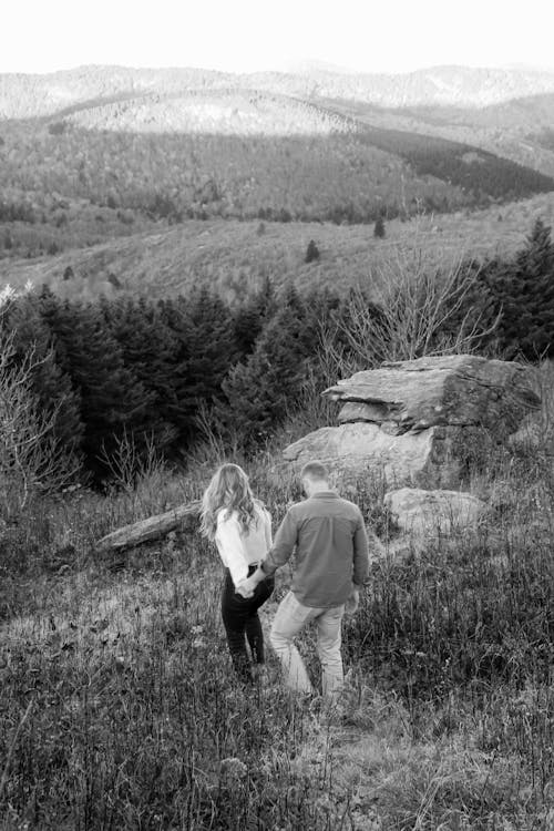 Grayscale Photo of a Man and a Woman Walking on Grass Field