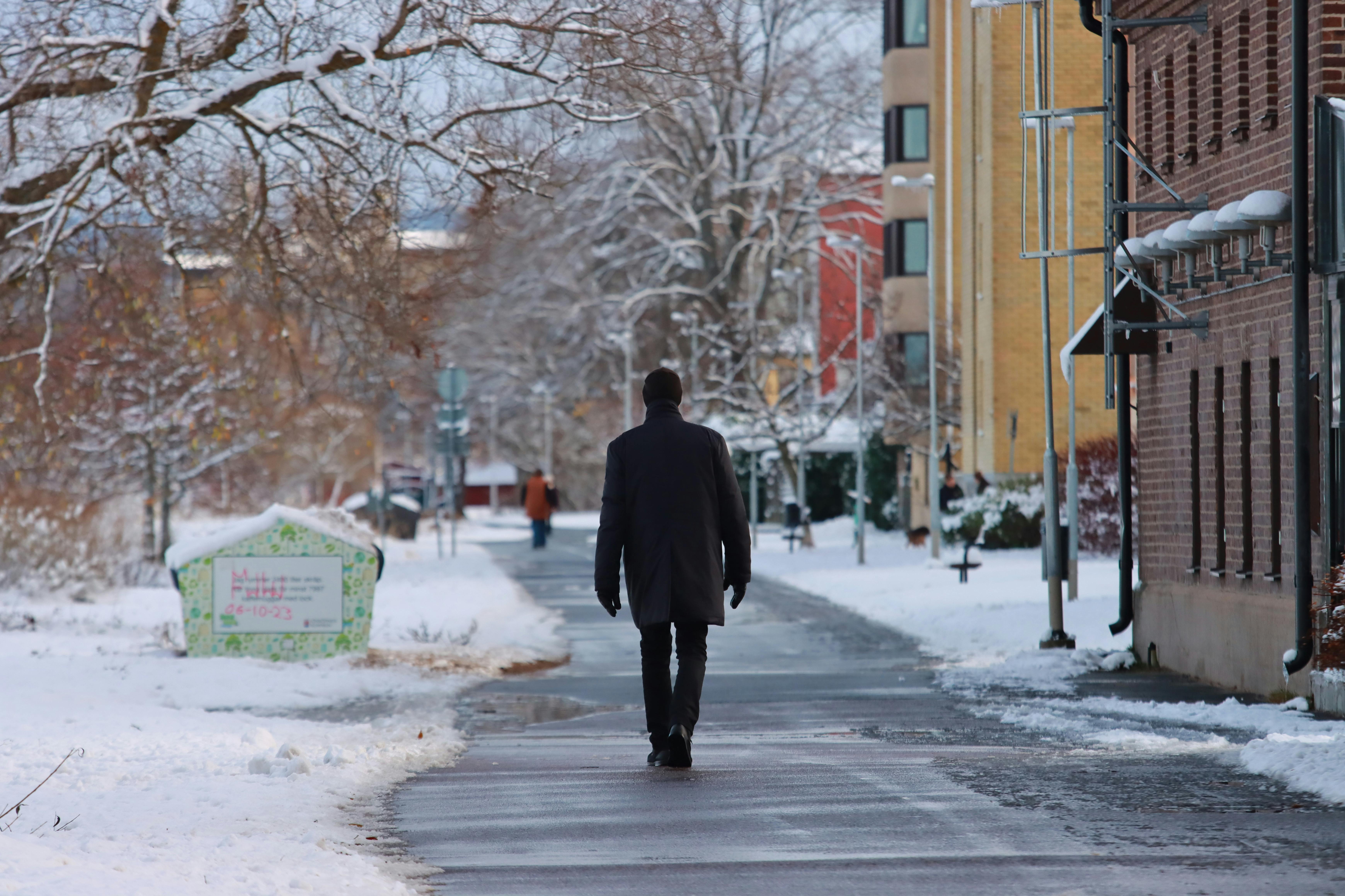 A Man in a Black Coat Walking on the Sidewalk on a Winter Day · Free