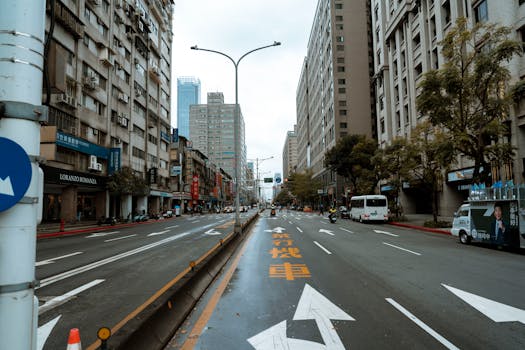 A bustling urban street scene with high-rise buildings and vehicles on a cloudy day.