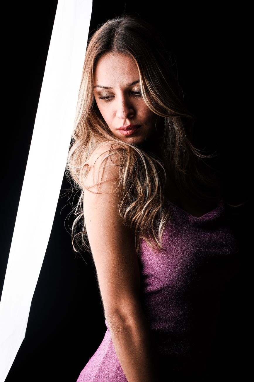 A young woman in a shimmering lilac dress posing with dramatic lighting in a studio.. pexels, young, woman