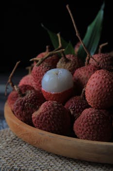 A close-up of fresh lychees with a peeled one in a wooden bowl for healthy food themes.