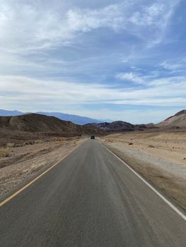 Empty road slicing through Death Valley, California, under a blue sky.