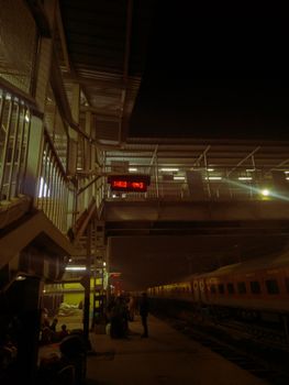 A bustling train station in Jammu at night with commuters and trains.