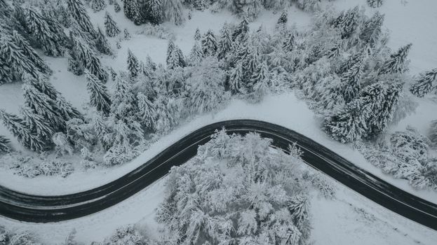 Curved snow-covered road through a frosty forest captured from above in winter.