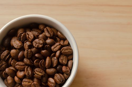 Free A top-view shot of roasted coffee beans in a ceramic bowl on a wooden table. Stock Photo