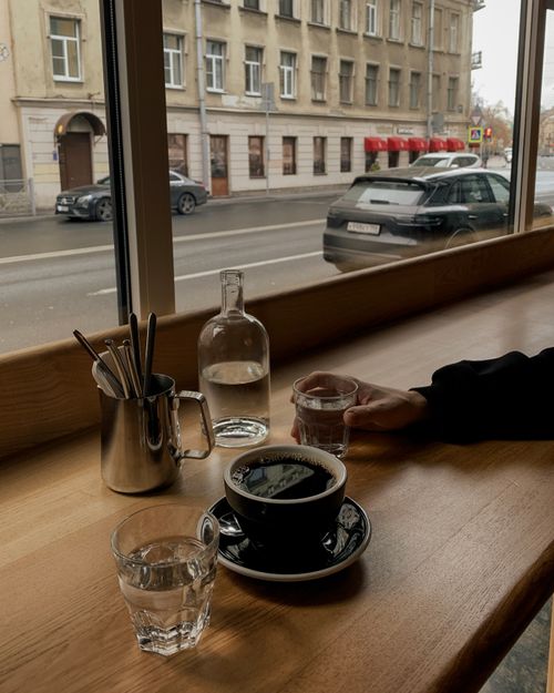 Free A relaxed moment by the café window with coffee, water, and a city street view. Stock Photo