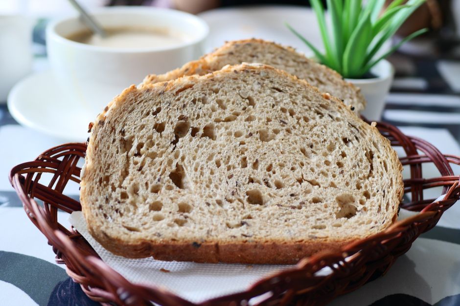 Close-up of rye bread slices in a basket with coffee and plant in the background.