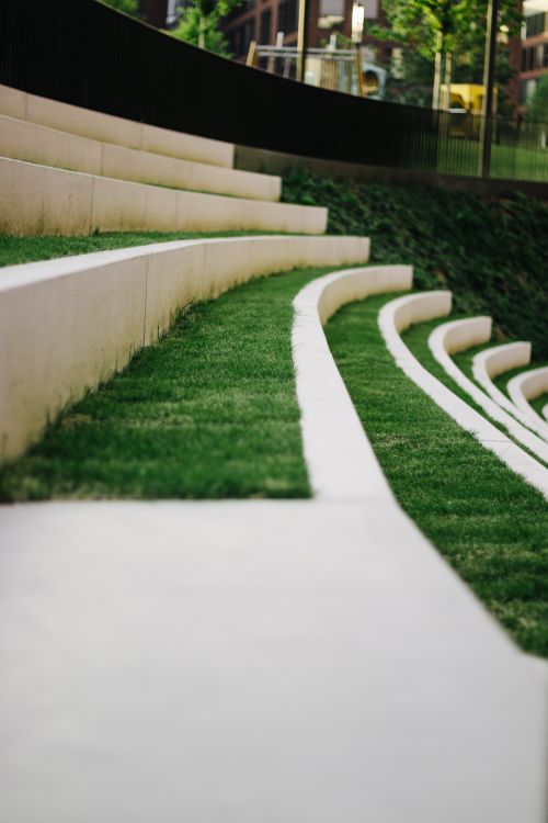 Free A serene close-up of a modern outdoor amphitheater with green grass and concrete seating. Stock Photo