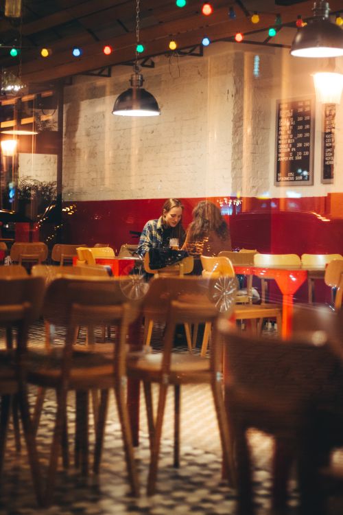 Free Two women enjoying a conversation in a warmly lit urban café. Stock Photo
