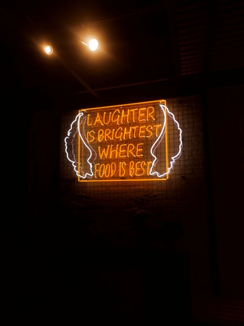 Free Orange neon sign with a cheerful message about laughter and food, emphasizing brightness. Stock Photo