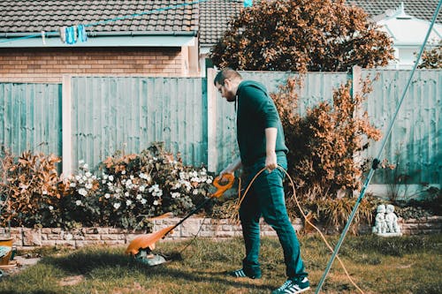 男子手持橙色电动割草机在草坪上