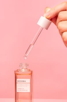 Close-up of a skincare oil bottle with pipette against a pink background, emphasizing elegance and self-care.