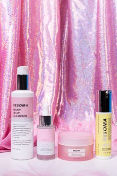 A selection of skincare products arranged against a pink holographic fabric backdrop, highlighting beauty and elegance.