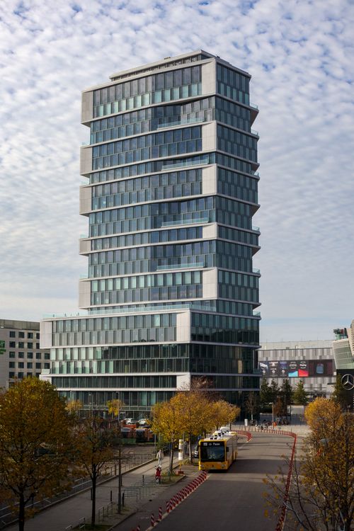 Free A tall modern skyscraper with a glass facade in Berlin, captured on a cloudy day with a bus on the street below. Stock Photo