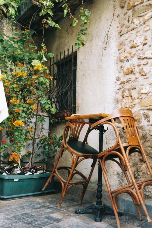 Free Cozy outdoor cafe scene with wooden chairs and rustic stone walls, creating a vintage European ambiance. Stock Photo