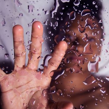 Artistic close-up of a woman's hand pressing against a wet glass surface with droplets.