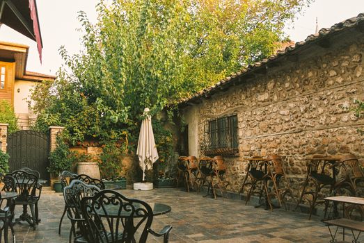 Charming rustic garden café featuring empty chairs, tables, stone wall, and lush greenery.