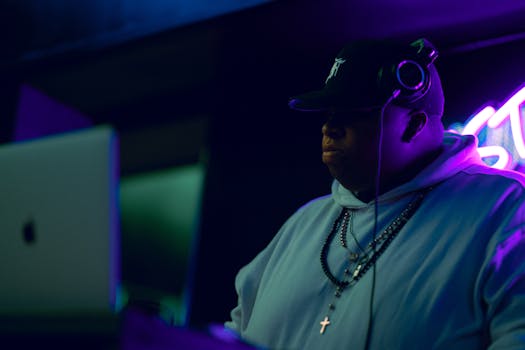 DJ performing in a dark room with neon lights, wearing headphones and a hoodie.