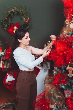 A woman decorates a Christmas tree with festive ornaments indoors.