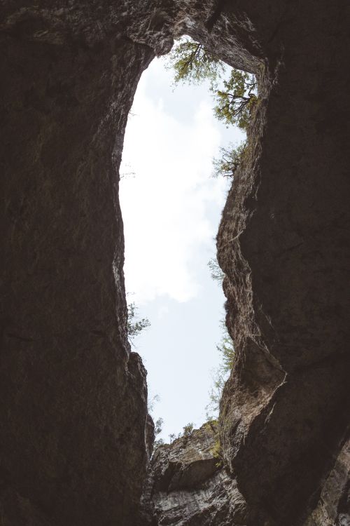 Free A stunning view of a cave opening revealing a clear blue sky and surrounding trees. Stock Photo