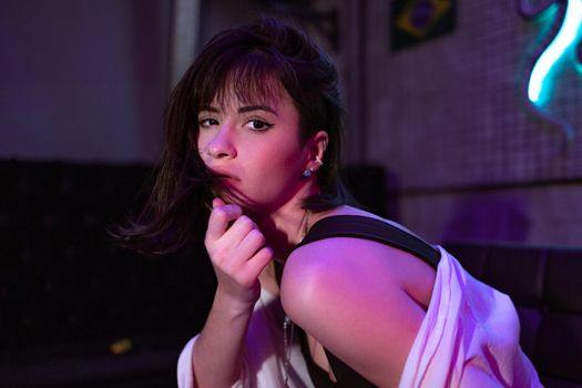 Portrait of a woman with dark hair in a neon-lit indoor setting, exuding modern style and confidence.