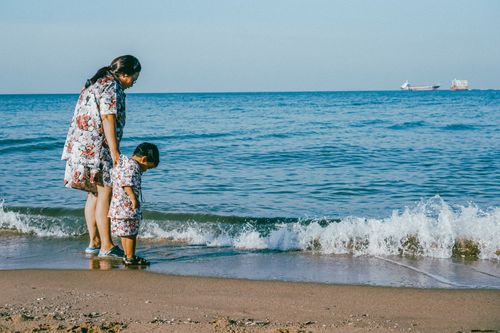 Free A woman and child enjoy a peaceful walk by the sea on a sunny day. Stock Photo