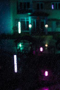 A moody urban night scene with raindrops on a window, backlit by neon lights.