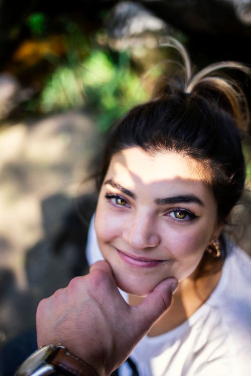 Free A smiling woman outdoors, looking up warmly, with sunlight casting shadows. Stock Photo