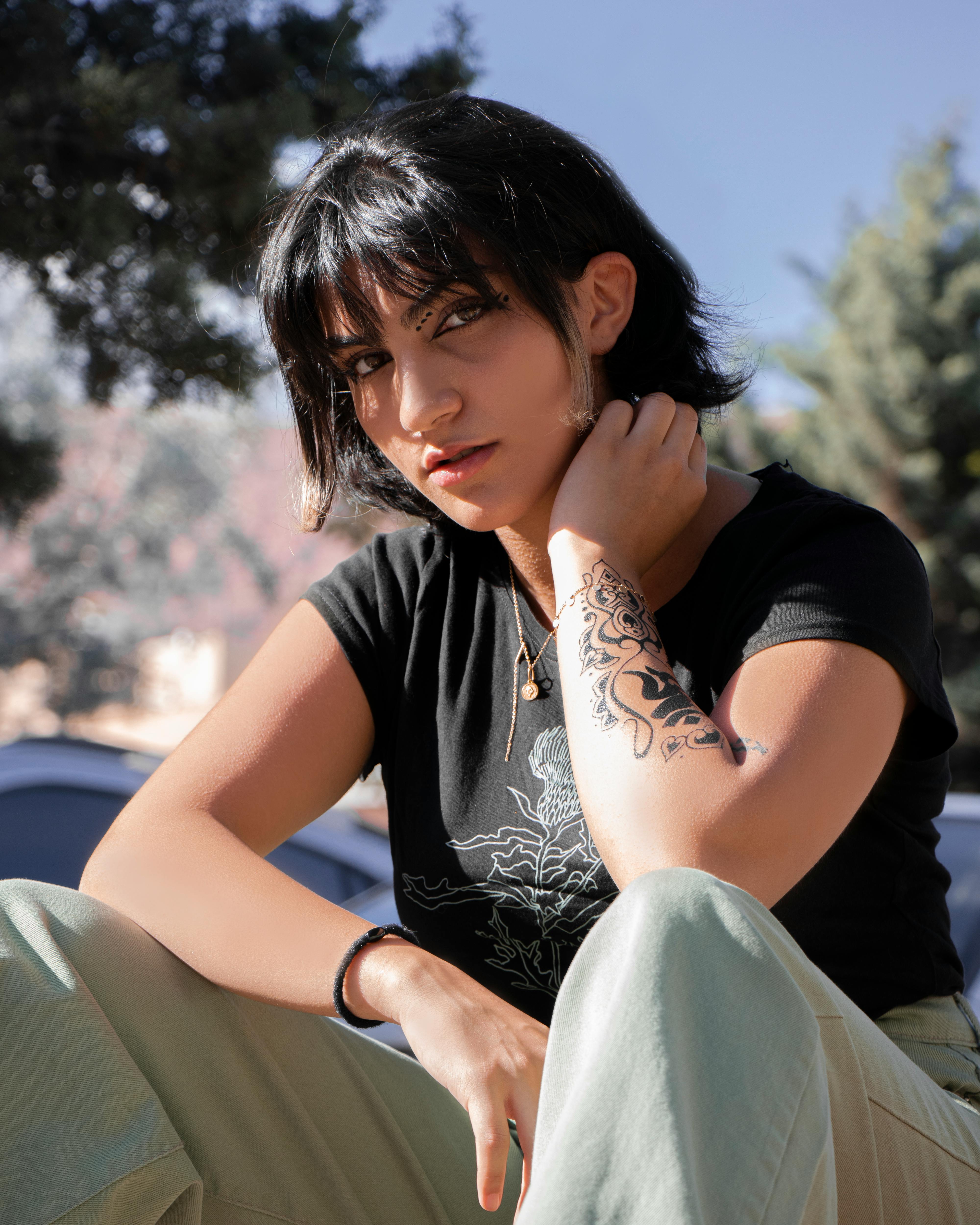 Stylish young woman with tattoo sitting outdoors on a sunny day.