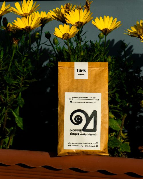 Free Coffee package displayed amidst bright yellow flowers in outdoor setting. Stock Photo