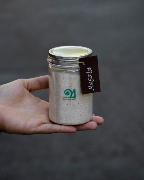 Free Close-up of a hand holding a glass jar filled with organic masala spice against a gray background. Stock Photo
