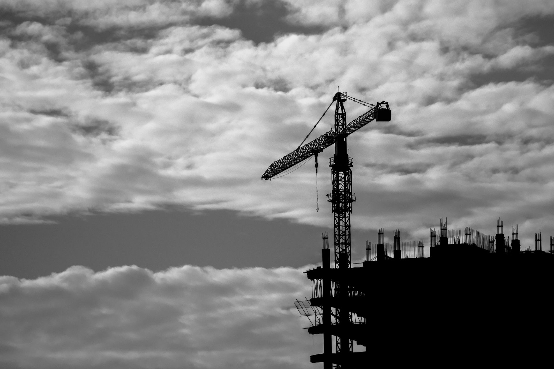 Silhouette of a tower crane and building under a cloudy sky, perfect for construction and architecture themes.