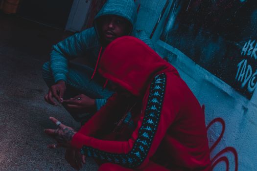 Two men in hoodies sit against a graffiti wall, exuding urban style.
