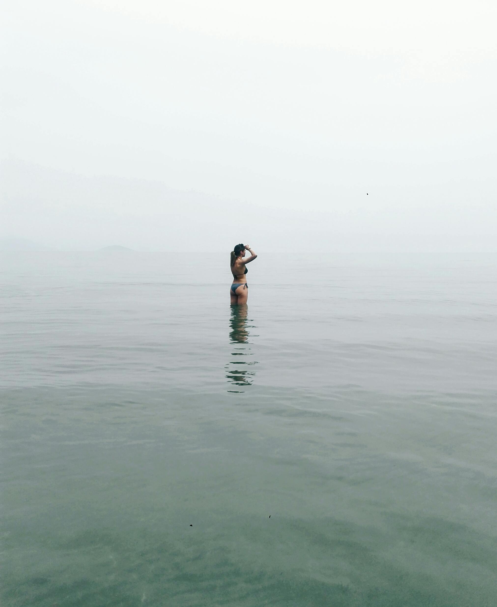 黄昏时分，一个人孤独地站在宁静的海水中，唤起一种孤独和反思的感觉