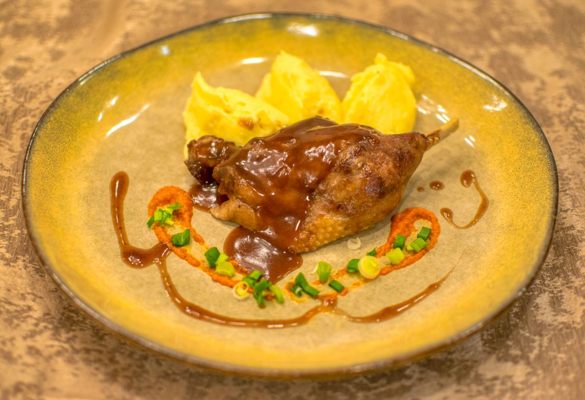 Slow-cooked duck leg served with rich brown sauce and creamy mashed potato on a rustic plate — the classic French bistro presentation of confit de canard.