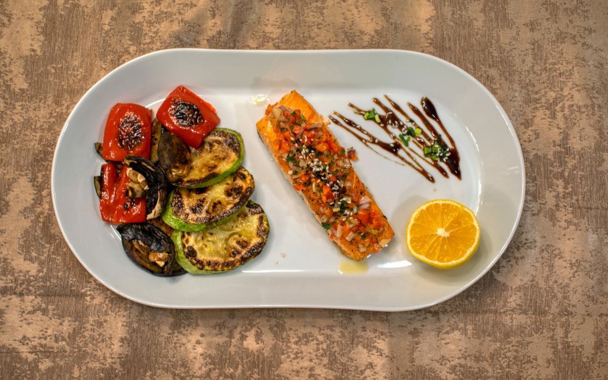 Gourmet grilled salmon served with roasted vegetables and lemon slice on a white plate.