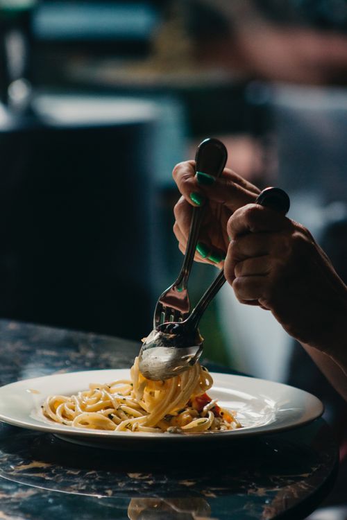 Free Hands twirling delicious pasta with fork and spoon on a plate, ready to eat. Stock Photo
