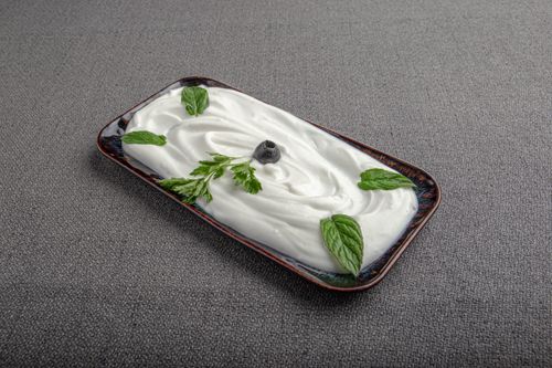 Free A close-up of whipped cream garnished with herbs and a blueberry on a decorative tray with gray background. Stock Photo