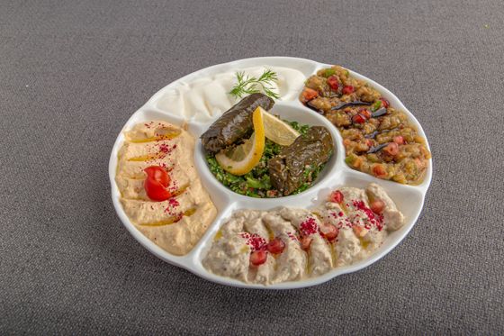 White divided platter with hummus, labneh, tabbouleh with stuffed grape leaves, eggplant salad and baba ganoush