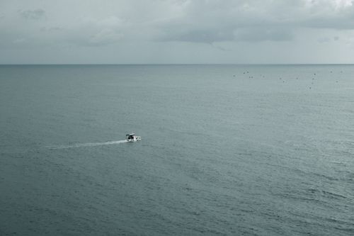 Free A solitary motorboat sails on a vast, calm sea under a cloudy sky, capturing serenity. Stock Photo
