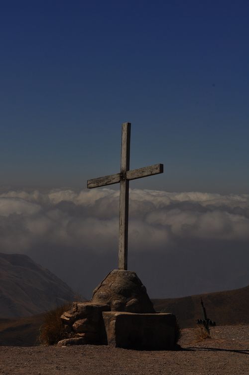 Free A lone wooden cross stands on a mountain peak against a dramatic sky with clouds. Stock Photo