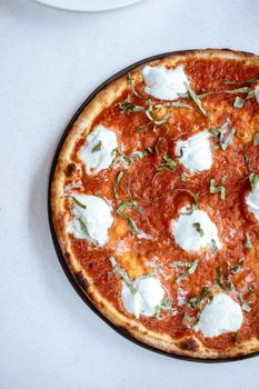 Top view of a tasty Margherita pizza with fresh mozzarella and basil on a white surface.