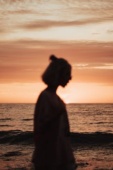 A serene silhouette of a woman against a sunset backdrop over the ocean, evoking tranquility.