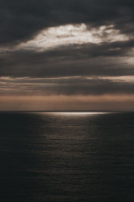 A moody ocean scene with dramatic clouds and light reflecting on the water at dusk.