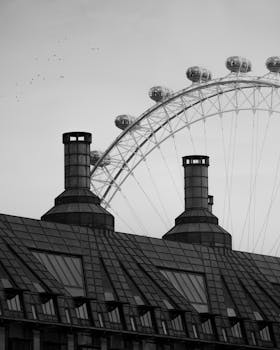 Dramatic black and white image of the London Eye towering over a building's rooftop in monochrome.