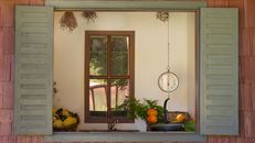 Rustic kitchen scene through window with scales, fruit, and herbs, exuding vintage charm.