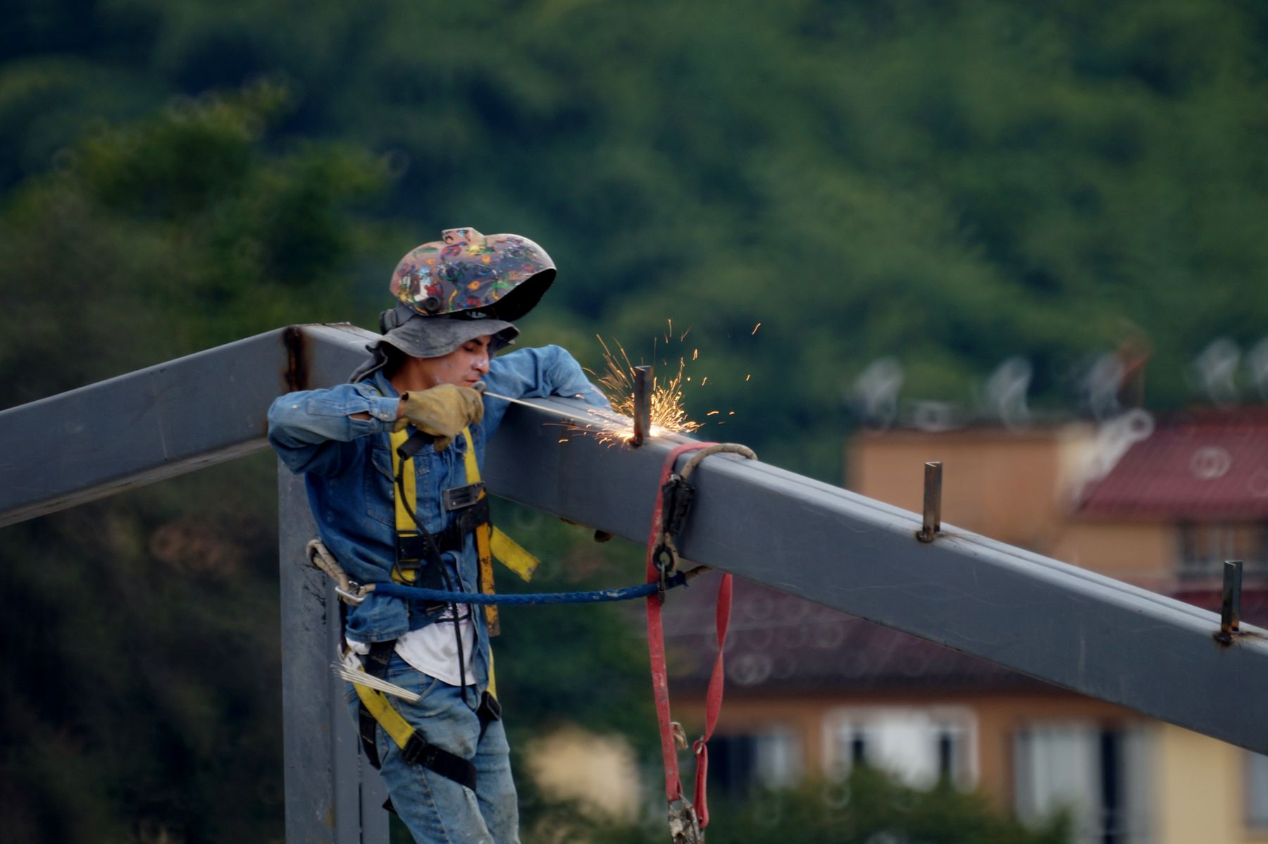 Steel erector working on a beam at height, sparks falling from a cut.