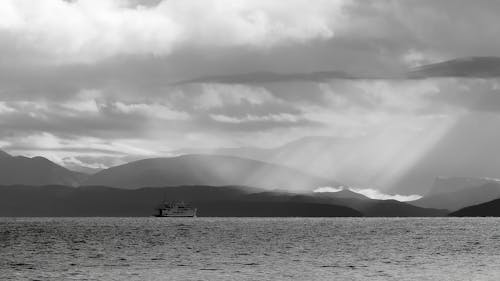 Grayscale Photo of a Ship on the Ocean under the Cloudy Sky